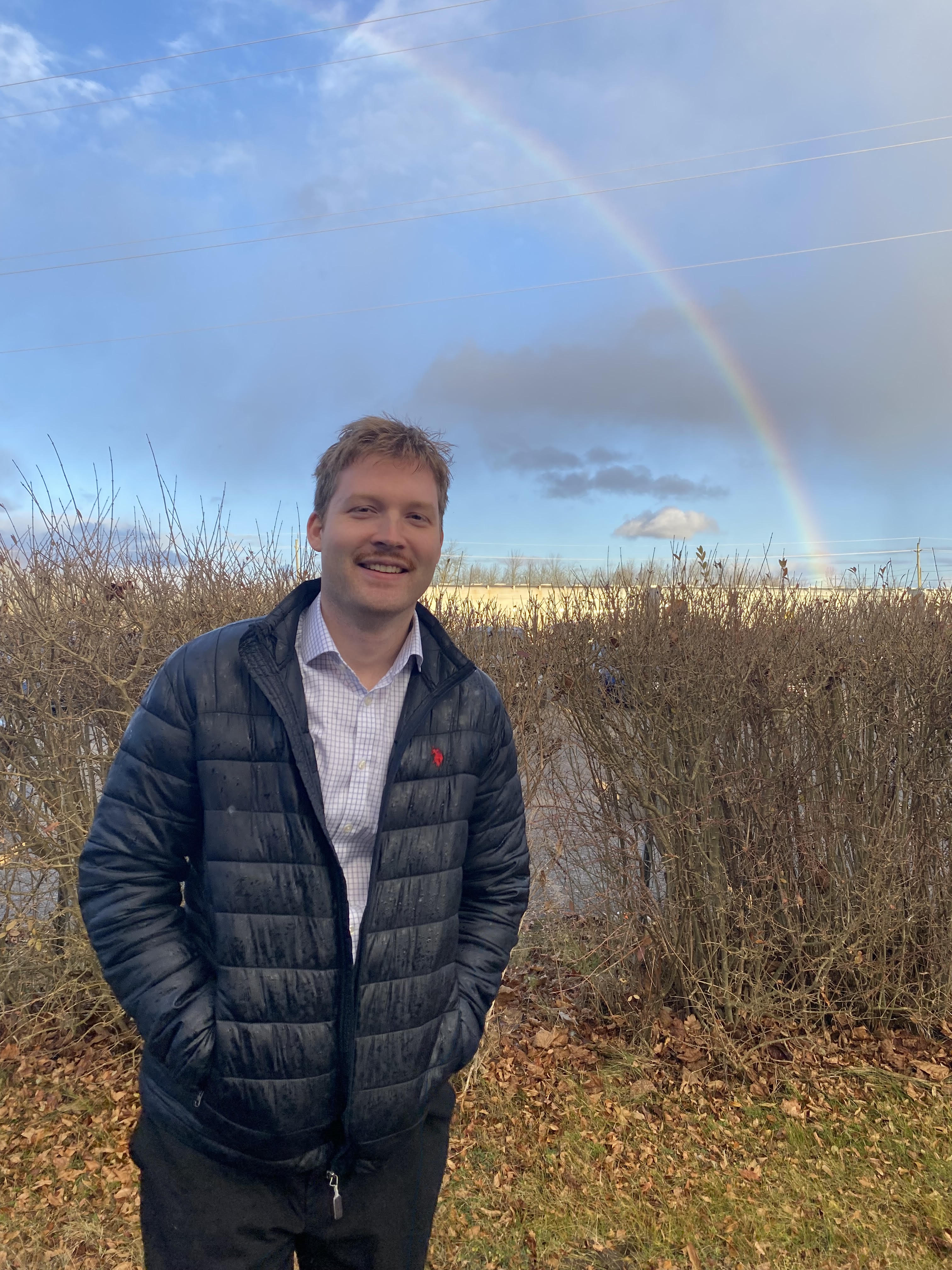 James Bell outdoors with a rainbow behind him